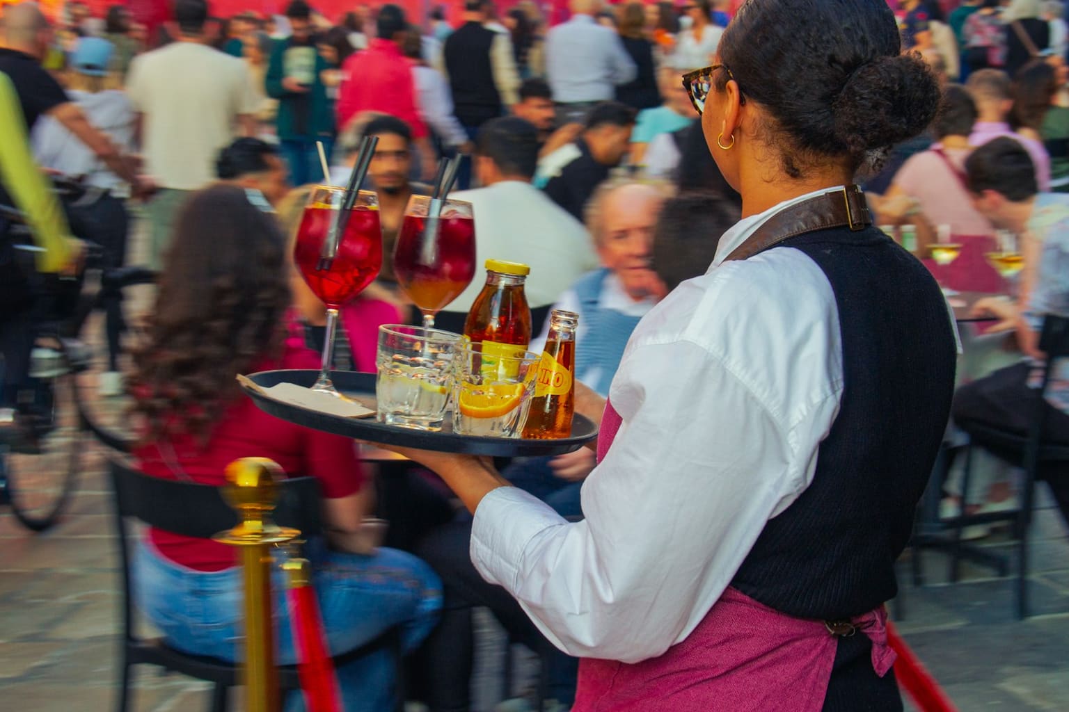 Waiter carrying a tray of drinks to guests on a busy terrace